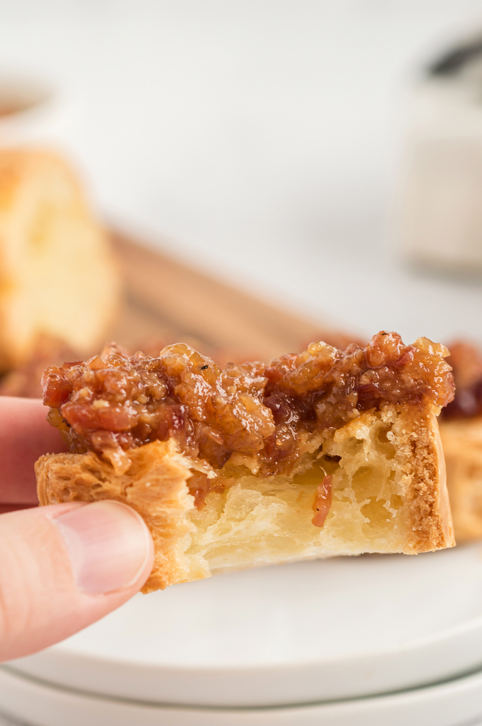 a person holding a piece of crostini topped with bacon jam