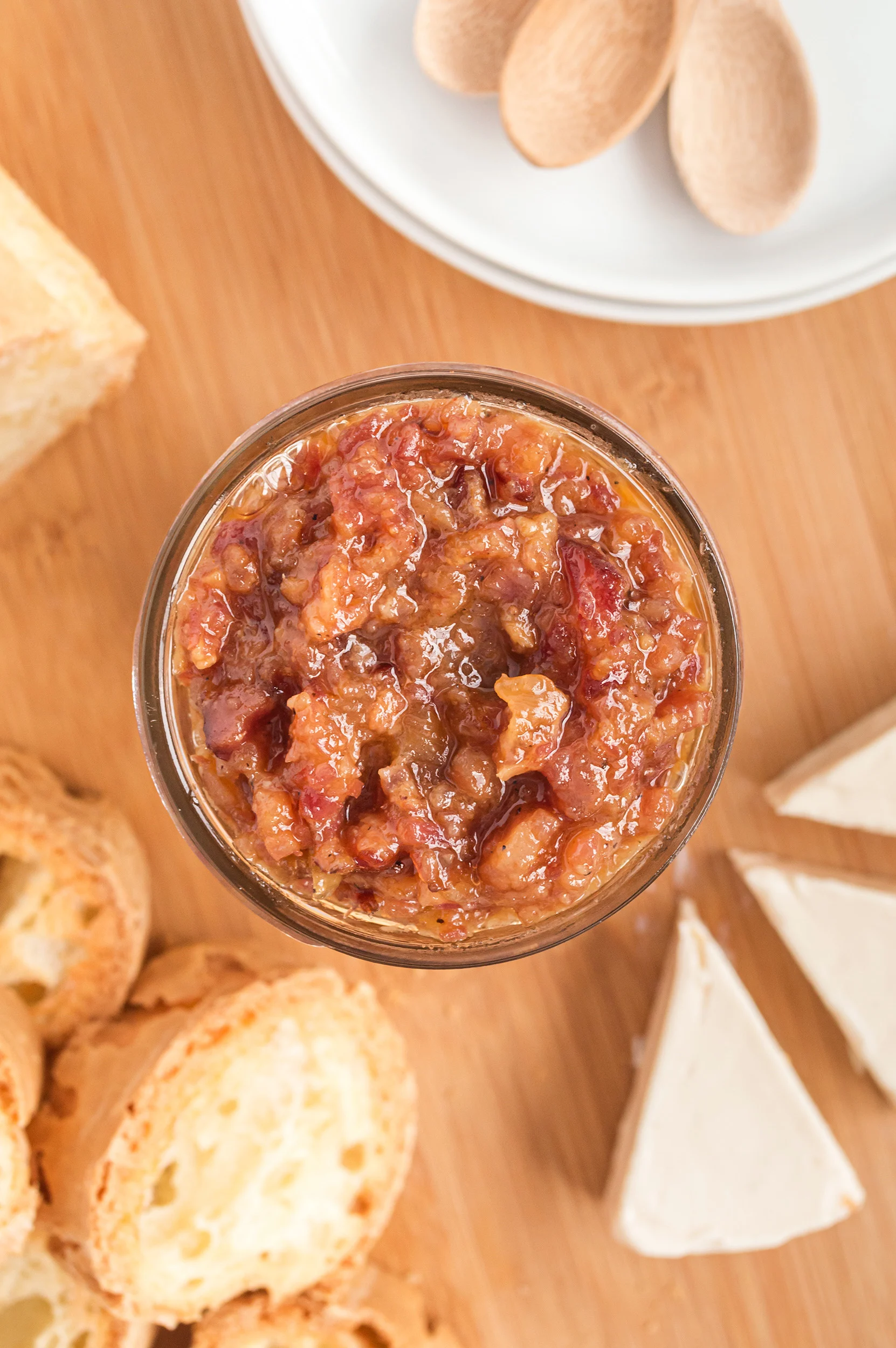 overhead photo of bacon jam in a mason jar next to brie wedges and toasted crostini