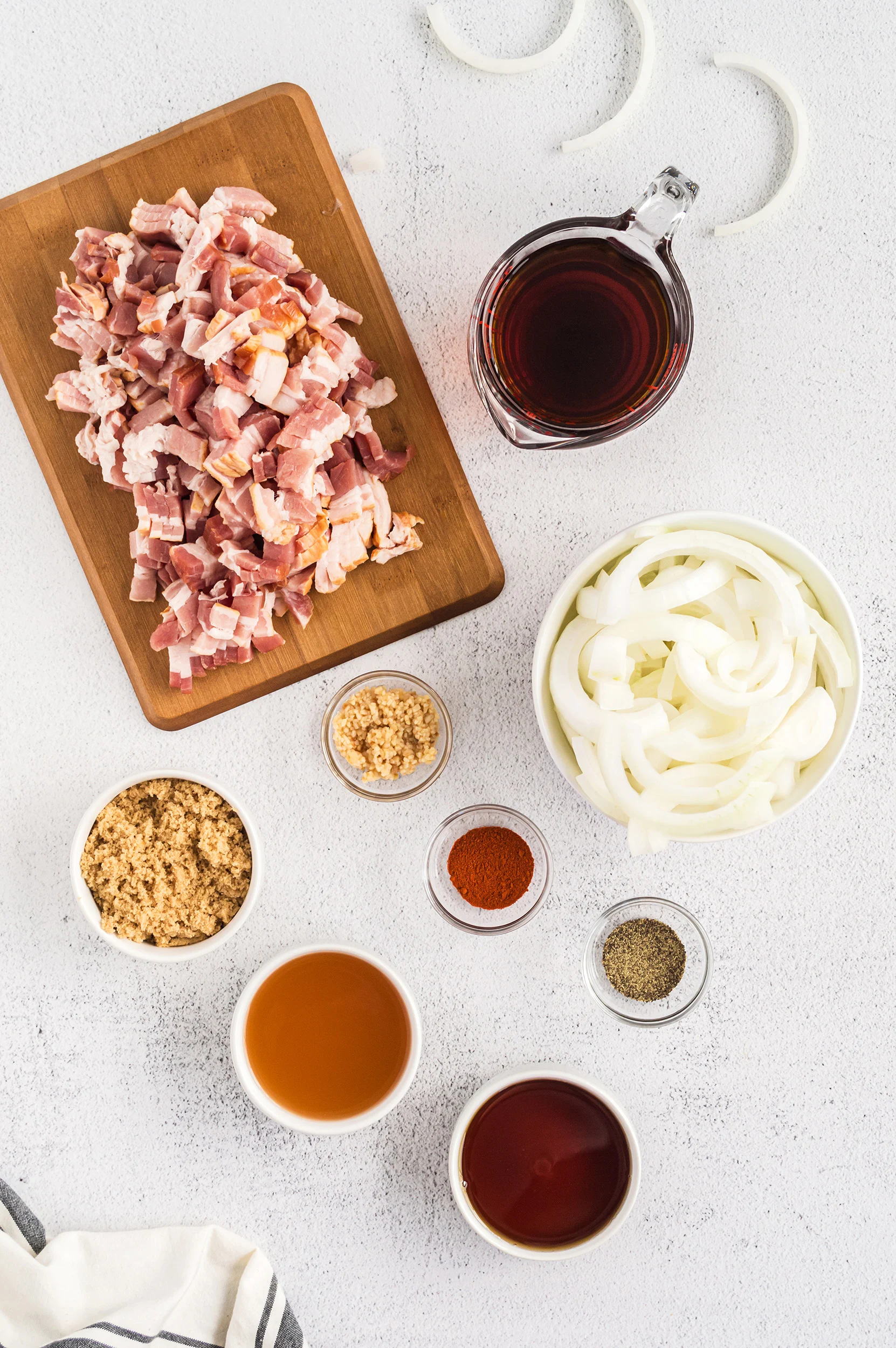 ingredients for bacon jam on a white background. all ingredients except the raw bacon are in containers and the bacon is on a cutting board
