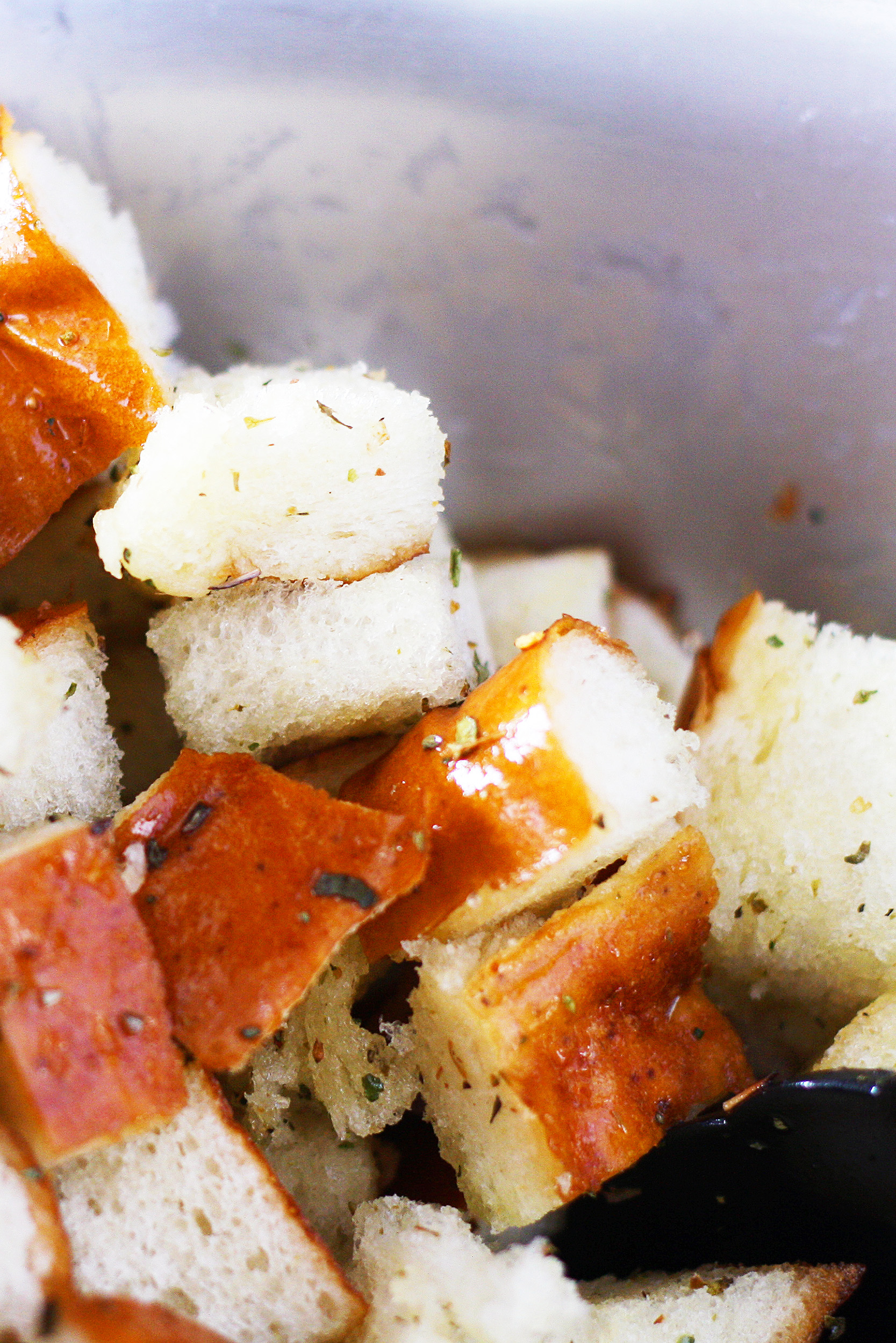 cubes of pretzel bread tossed with olive oil and spices in a metal mixing bowl