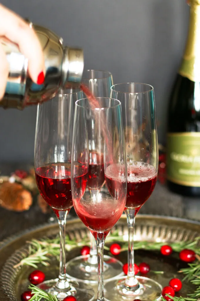 cranberry juice and vanilla vodka, chilled in a cocktail shaker, being poured into 4 champagne flutes