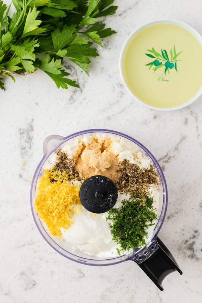 all ingredients for whipped feta dip, except the olive oil, in a food processor. the olive oil is in a small bowl above the food processor