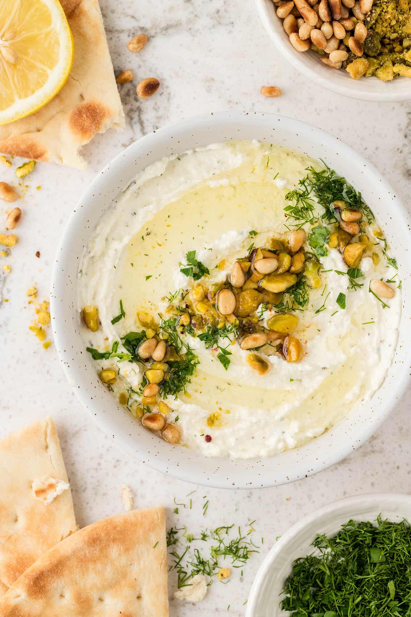 whipped greek feta dip in a white bowl with garnishes and pita chips 