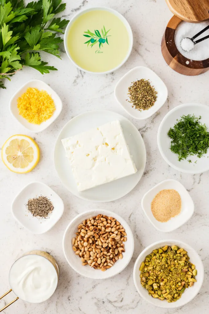 ingredients for whipped feta dip, in small white bowls on a marble countertop