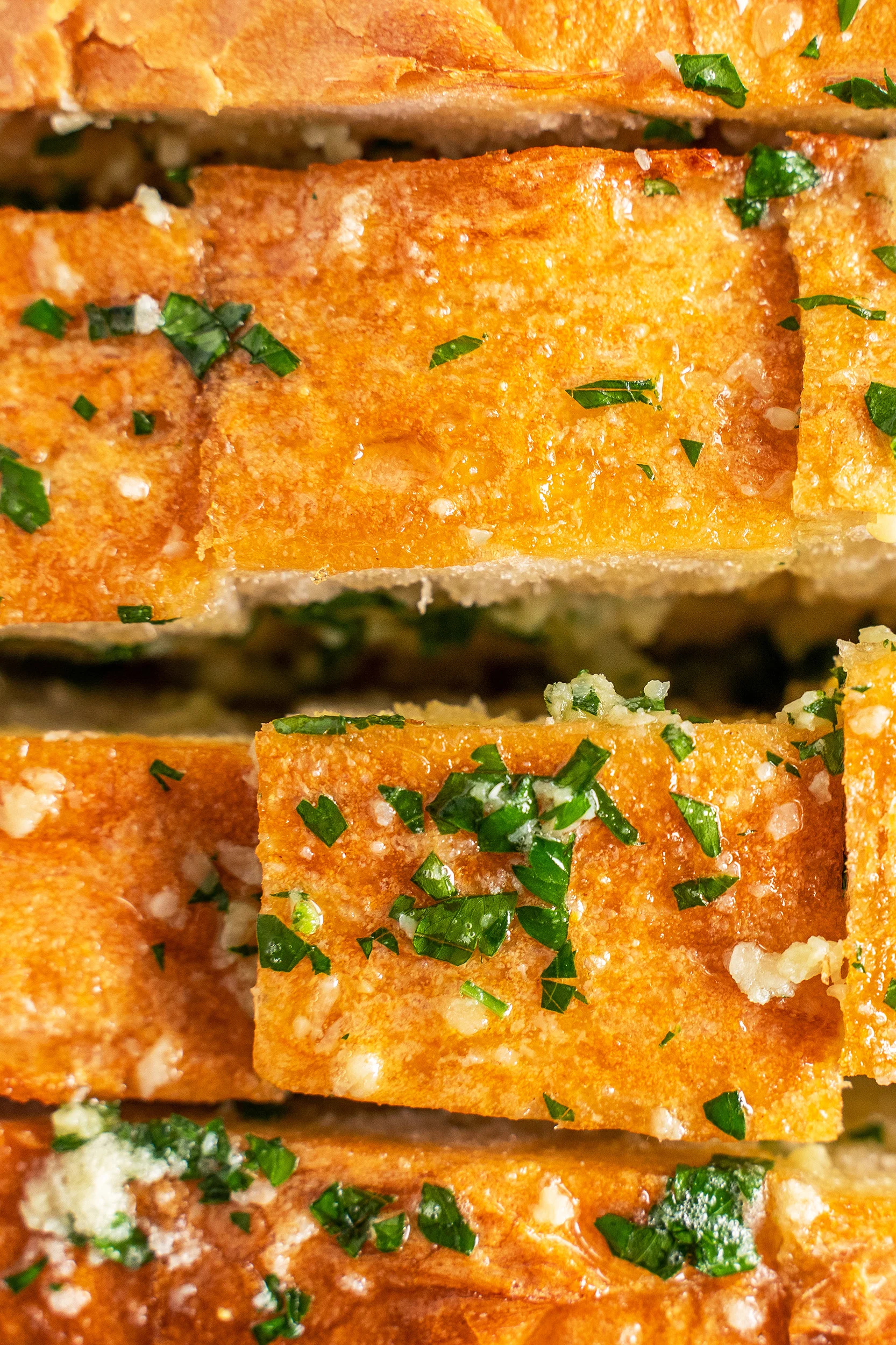 garlic butter mixture on top of bread loaf and in the cracks of the cut loaf