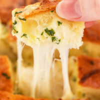 a person's hand pulling a piece of pull apart bread from the hot loaf