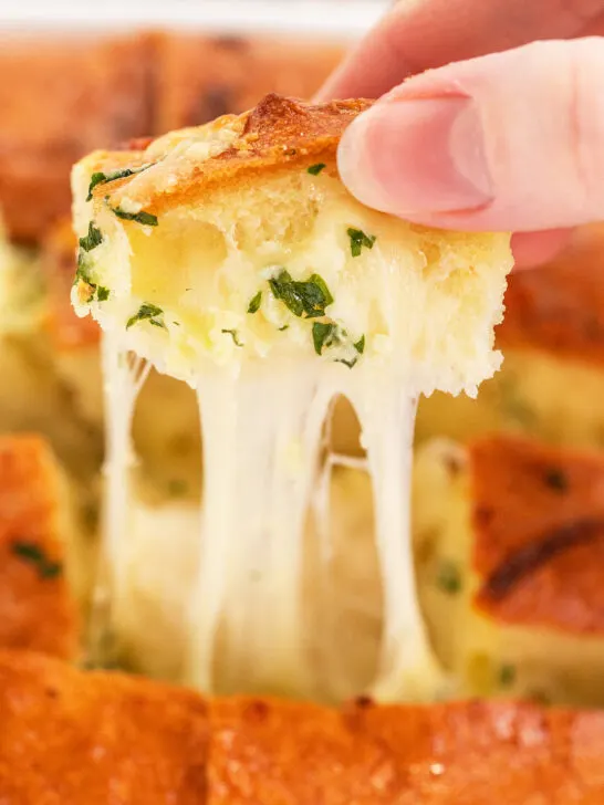 a person's hand pulling a piece of pull apart bread from the hot loaf