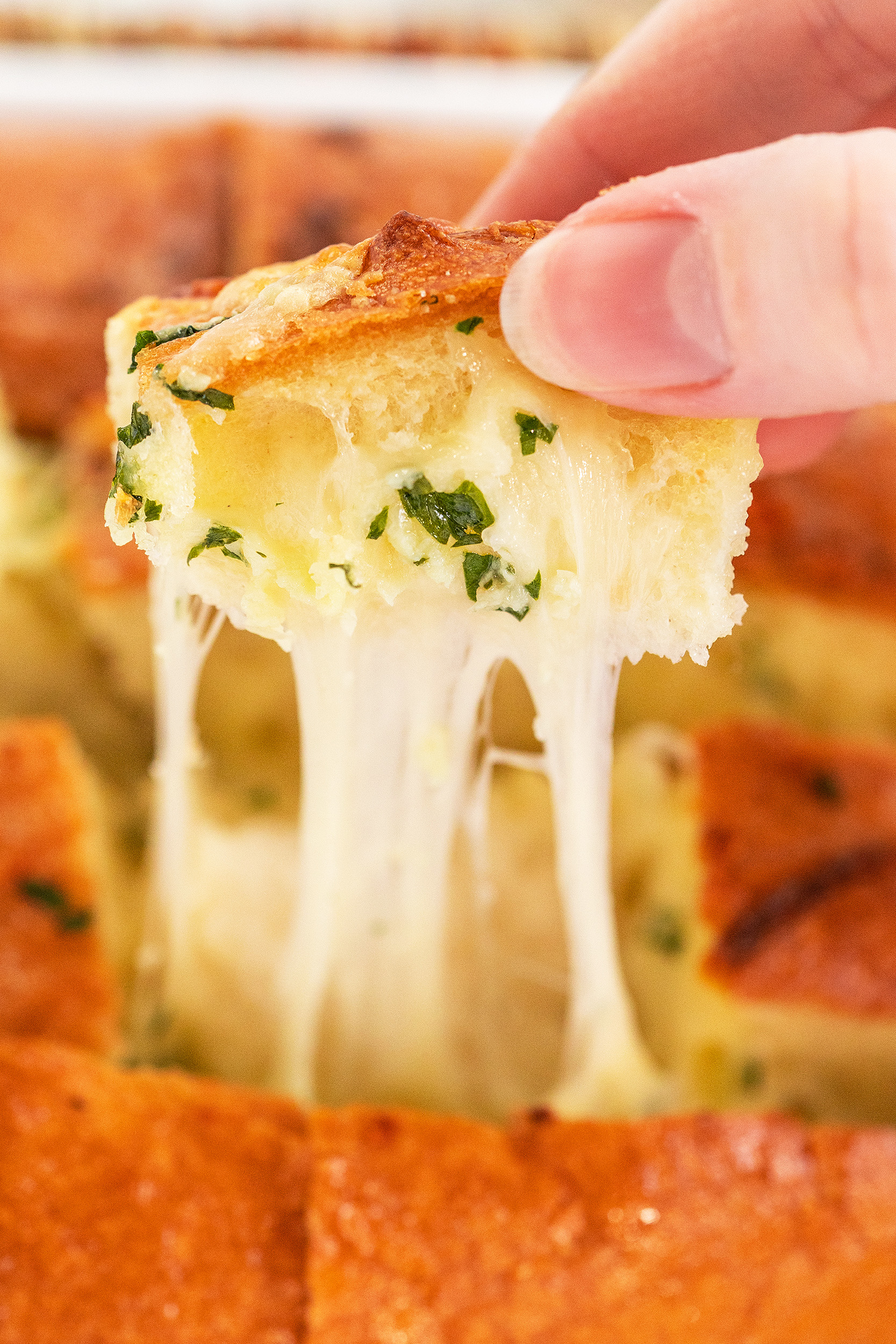 a person's hand pulling a piece of pull apart bread from the hot loaf