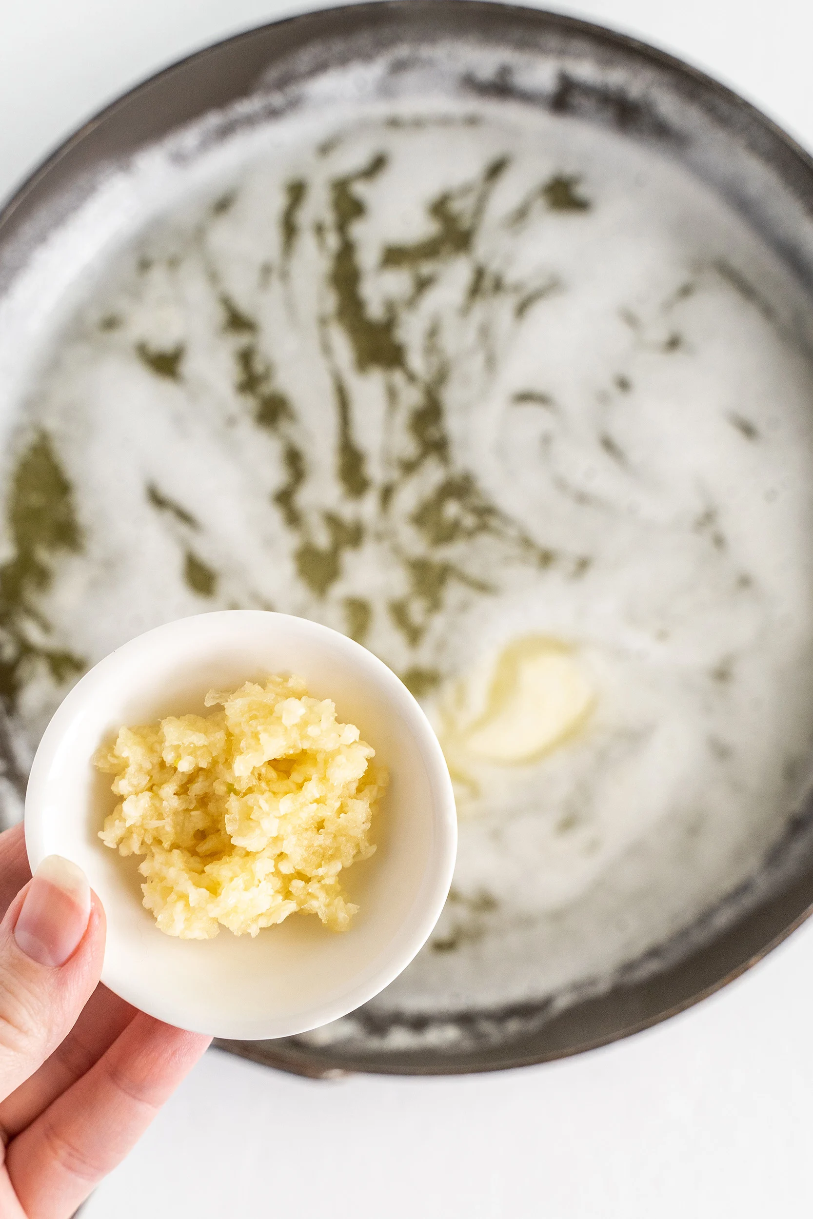 minced garlic in a small bowl being held over a pan of melted butter