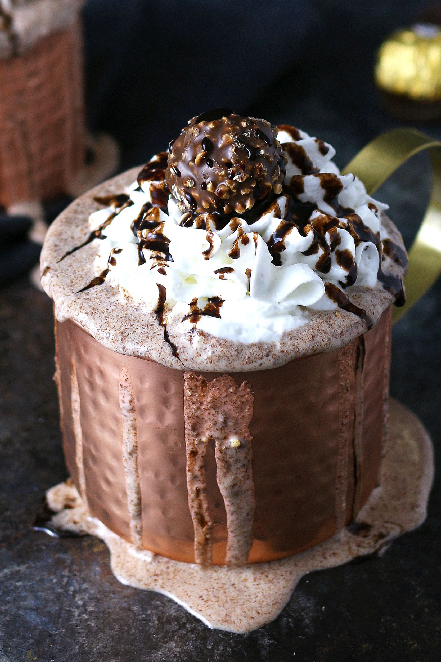 ferrero rocher nutella milkshake in a copper mug, it is overfilled and topped with whipped cream, chocolate syrup and 1 Ferrero rocher candy