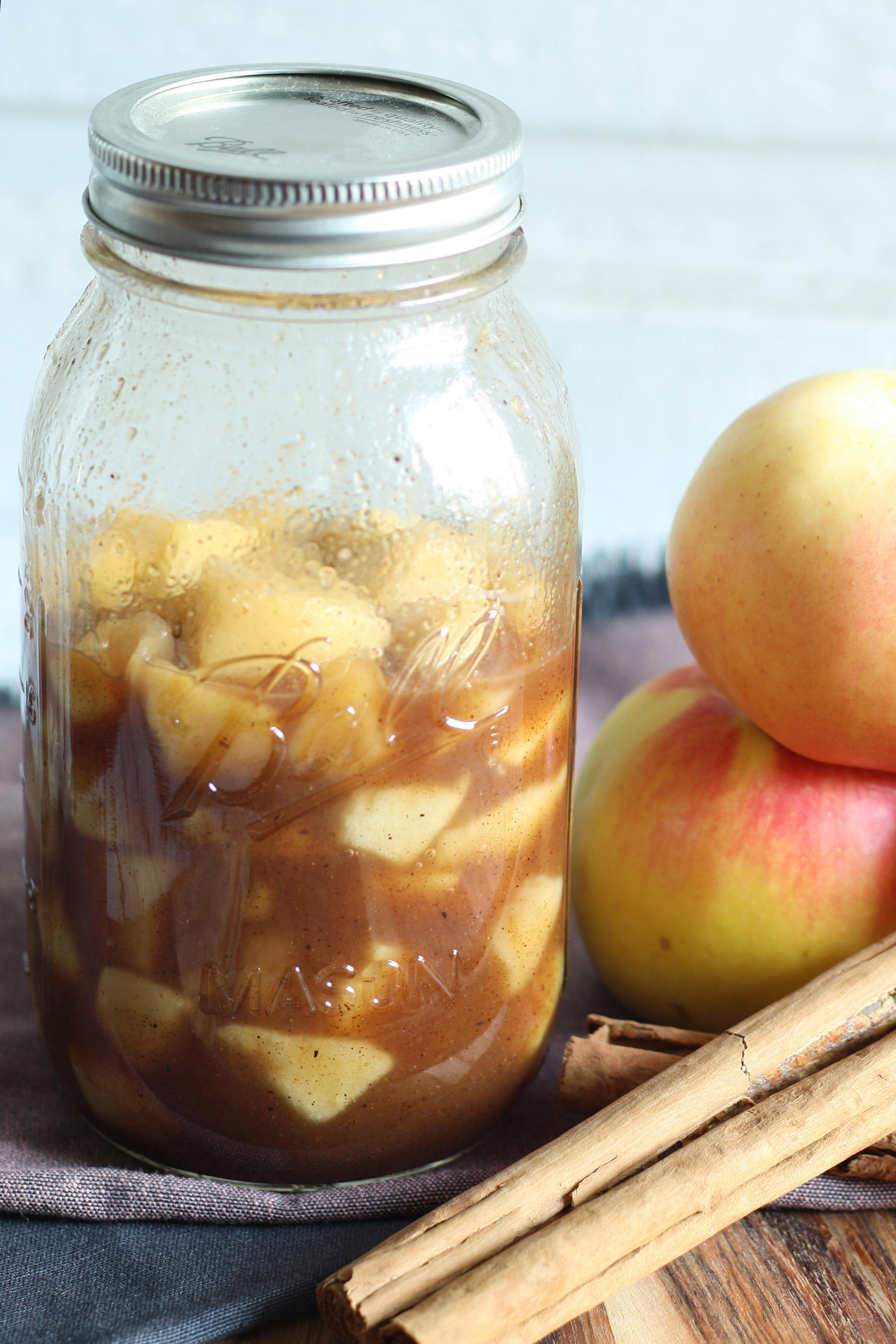 homemade apple pie filling without cornstarch in a mason jar next to some apples and cinnamon sticks