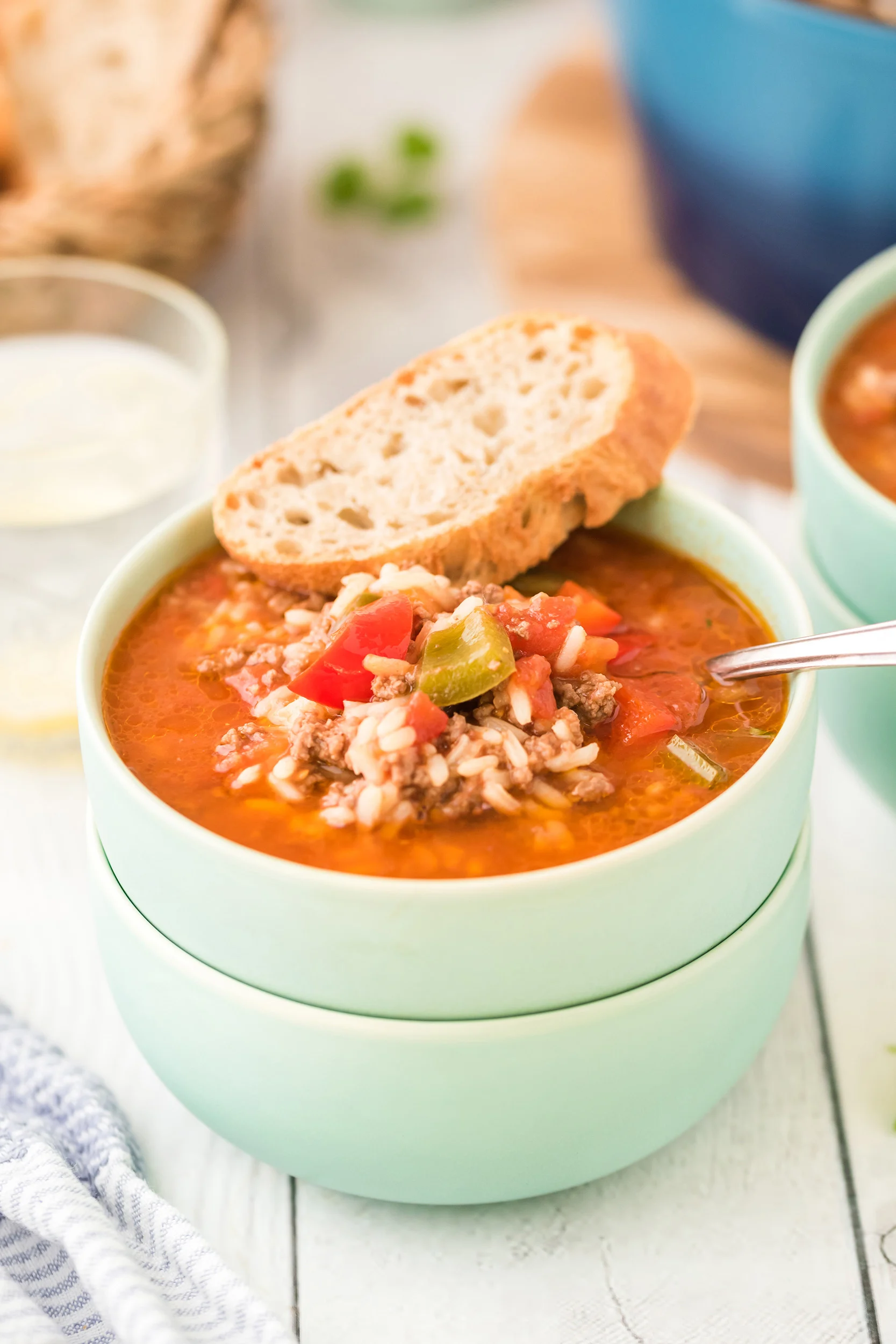 a mint green bowl of soup with a chunk of crusty bread on the rim of the bowl