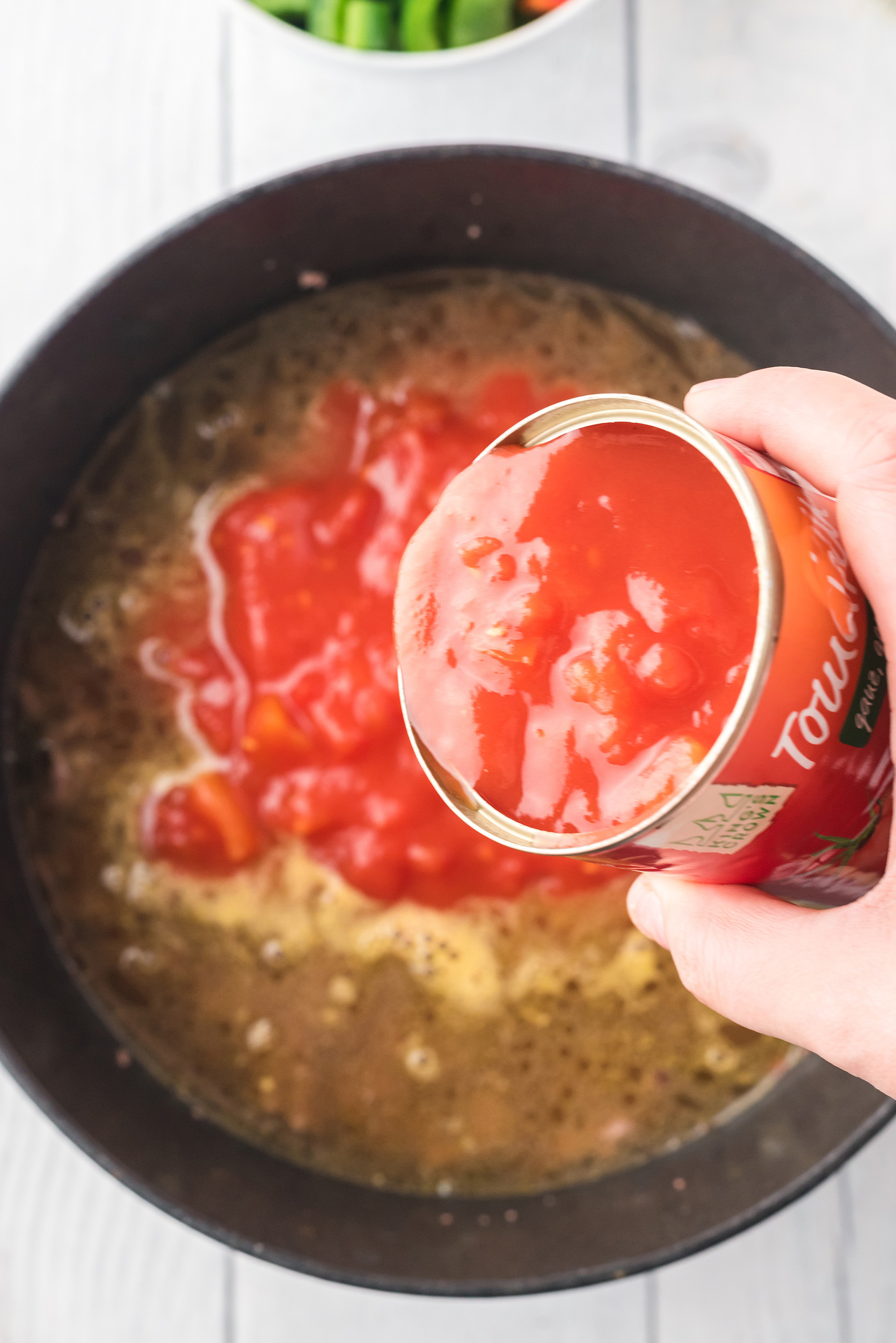 diced tomatoes and their liquid being added to the Dutch oven