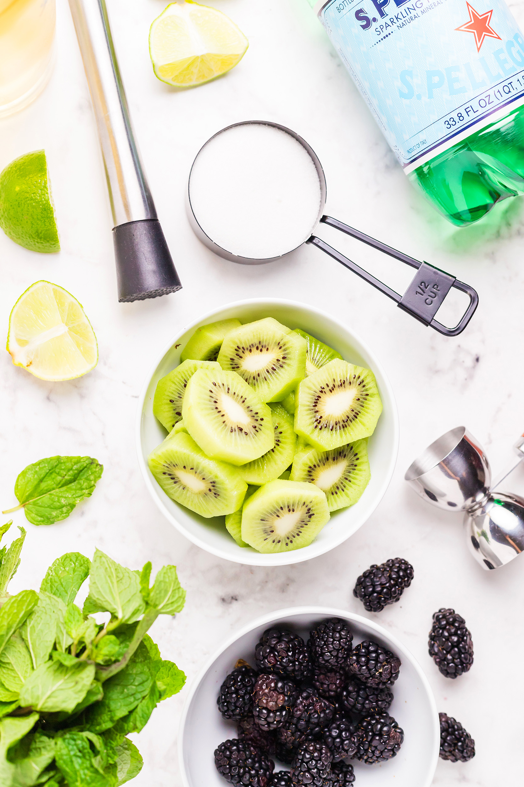 ingredients and tools for a blackberry kiwi mojito in small bowls and containers