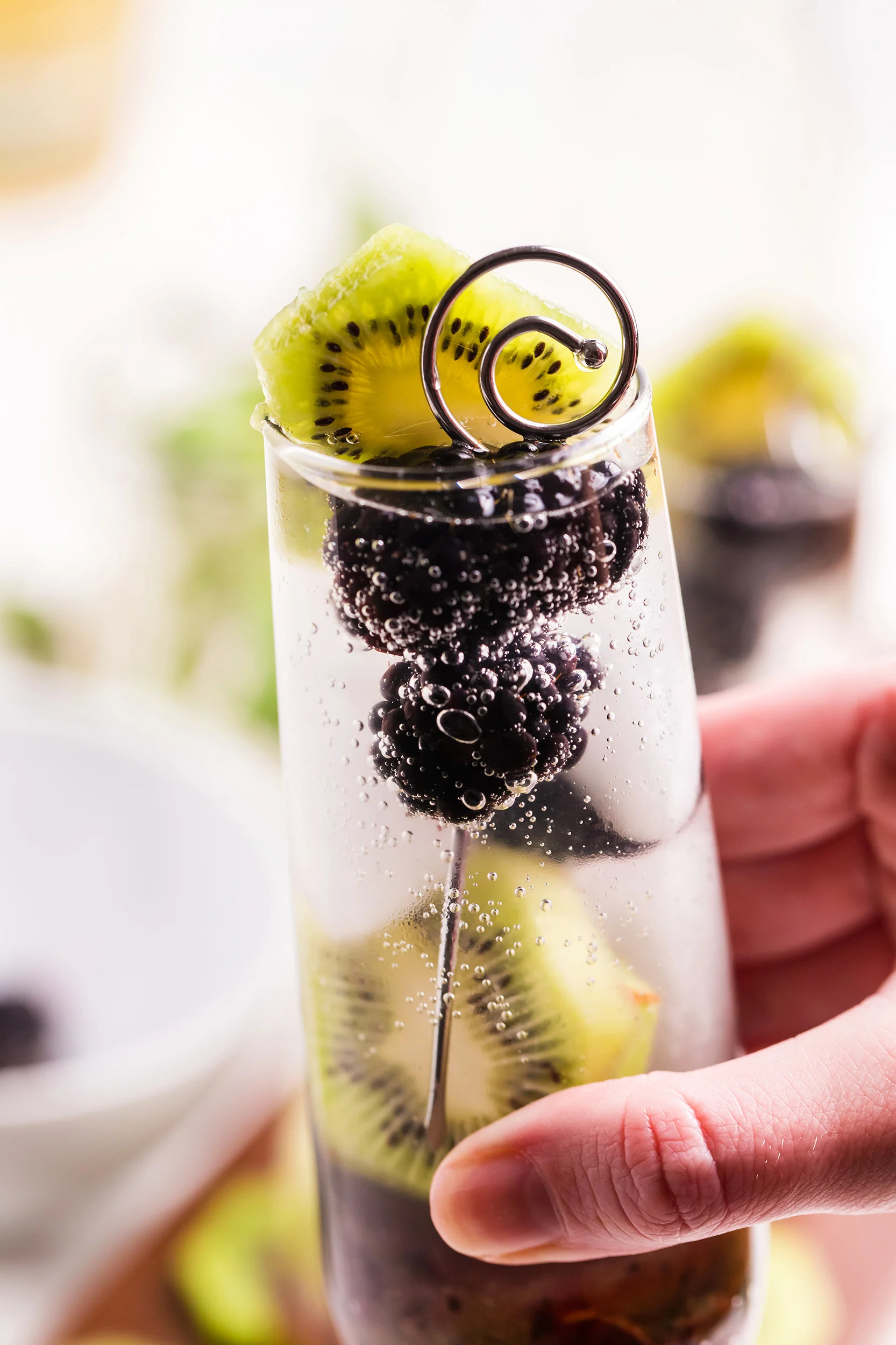 women's hand holding a blackberry kiwi mojito