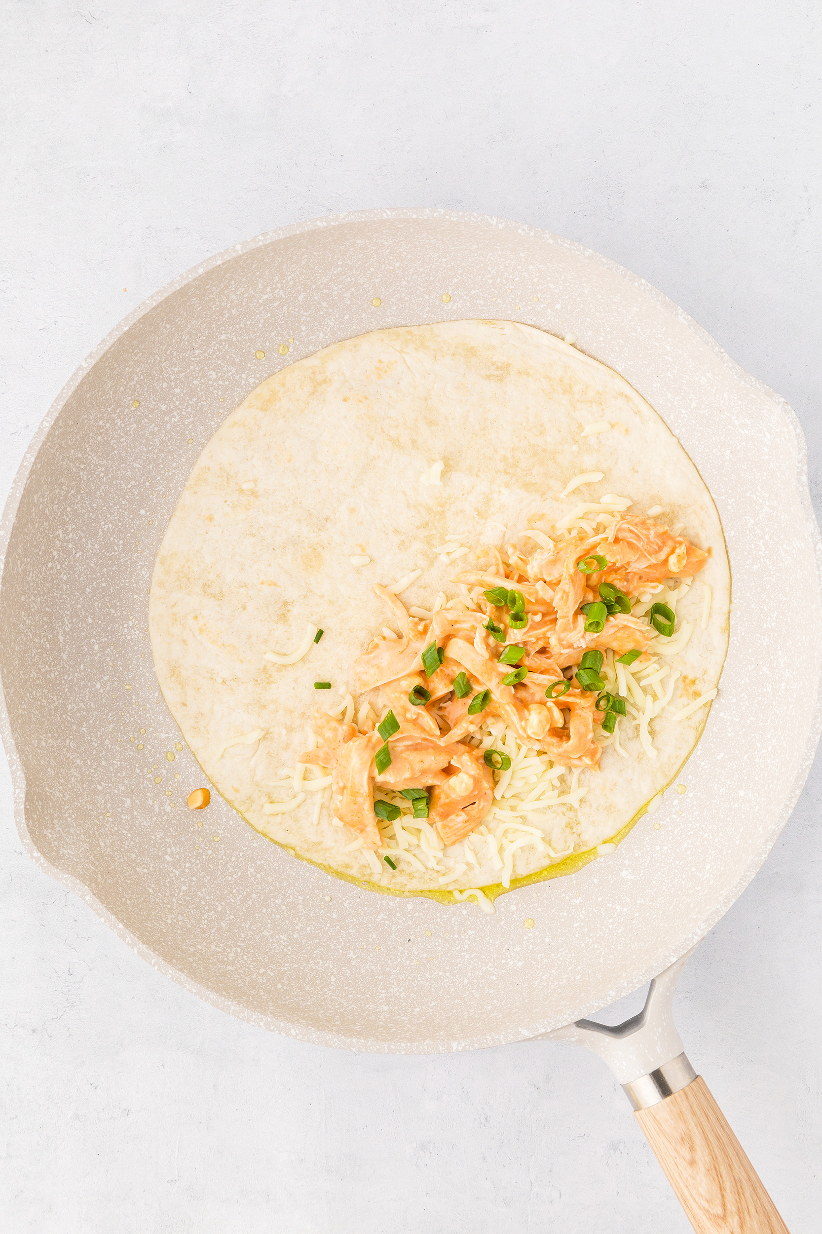 flour tortilla on a white skillet topped with buffalo chicken, cheese and green onion