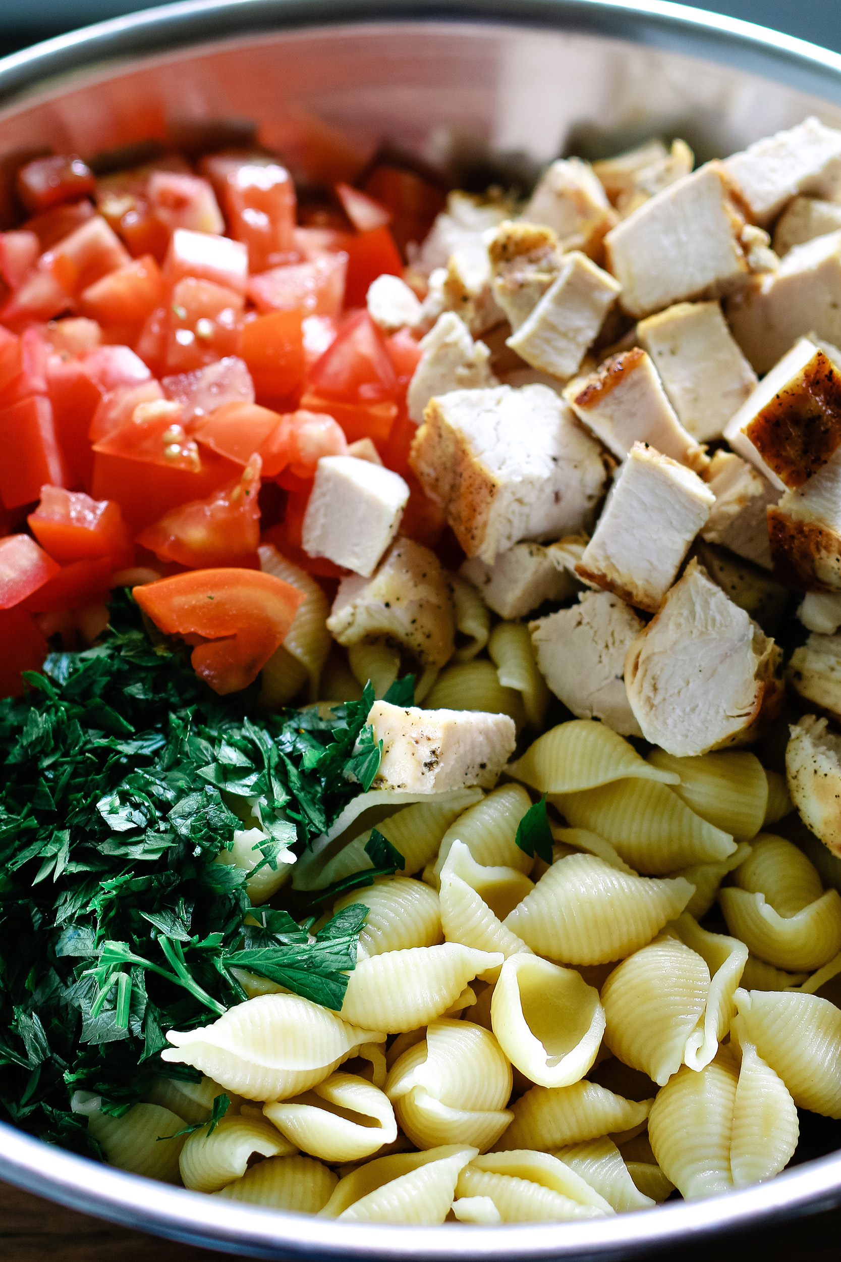 grilled chicken, parsley, pasta shells and diced tomatoes in a stainless steel bowl