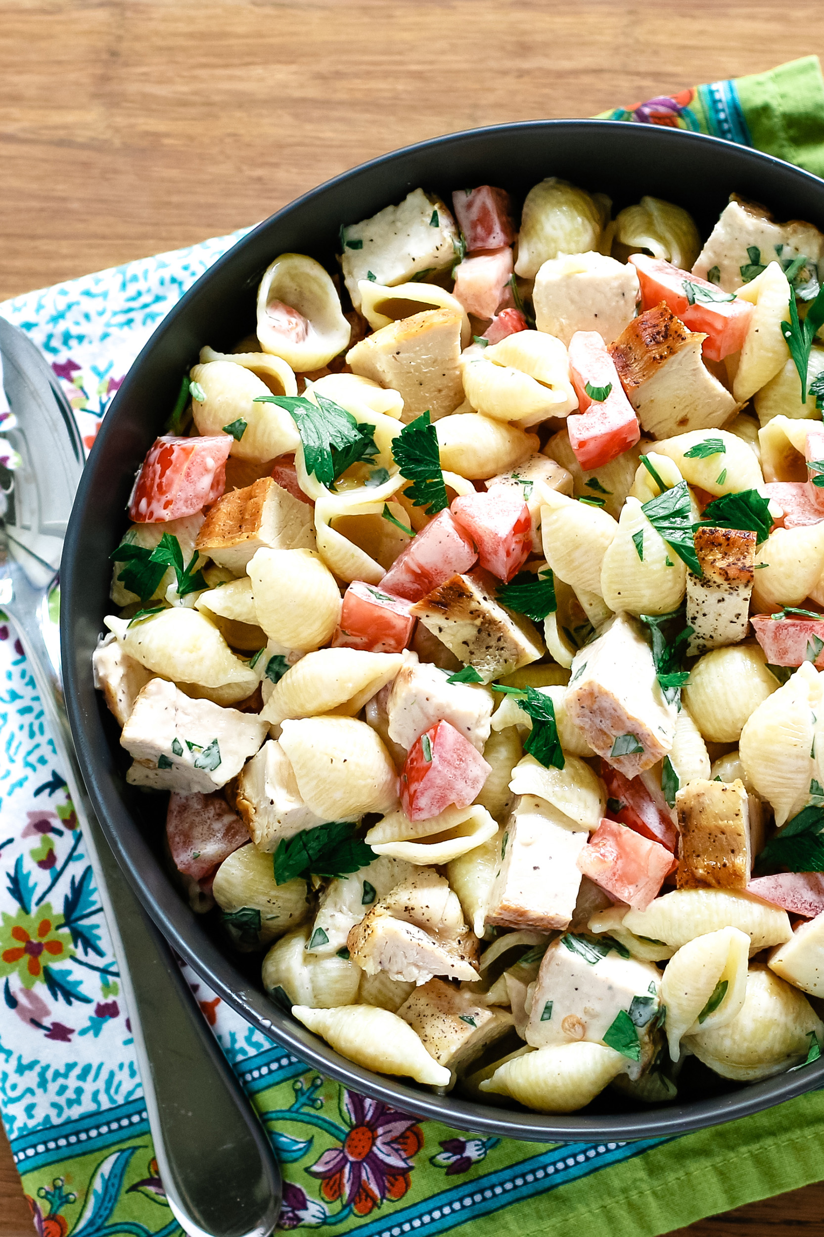 tossed chicken ranch pasta salad in a serving bowl on a wooden cutting board and a colorful napkin