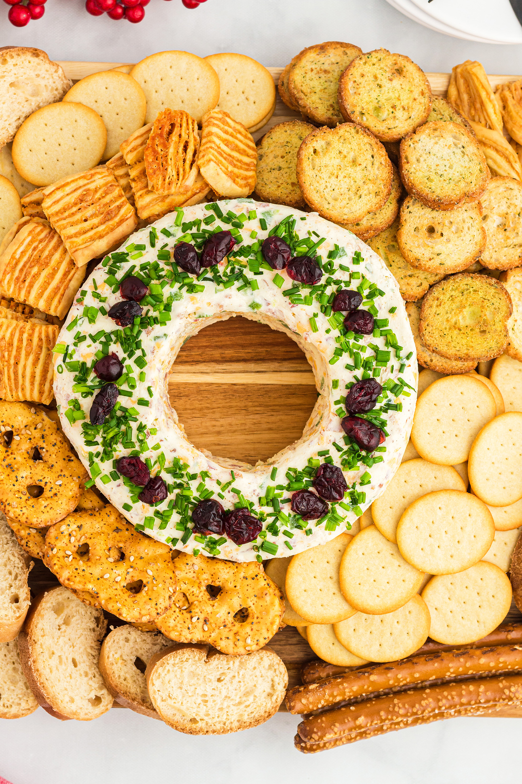 large wooden board with a cheese ball wreath in the center surrounded by crackers