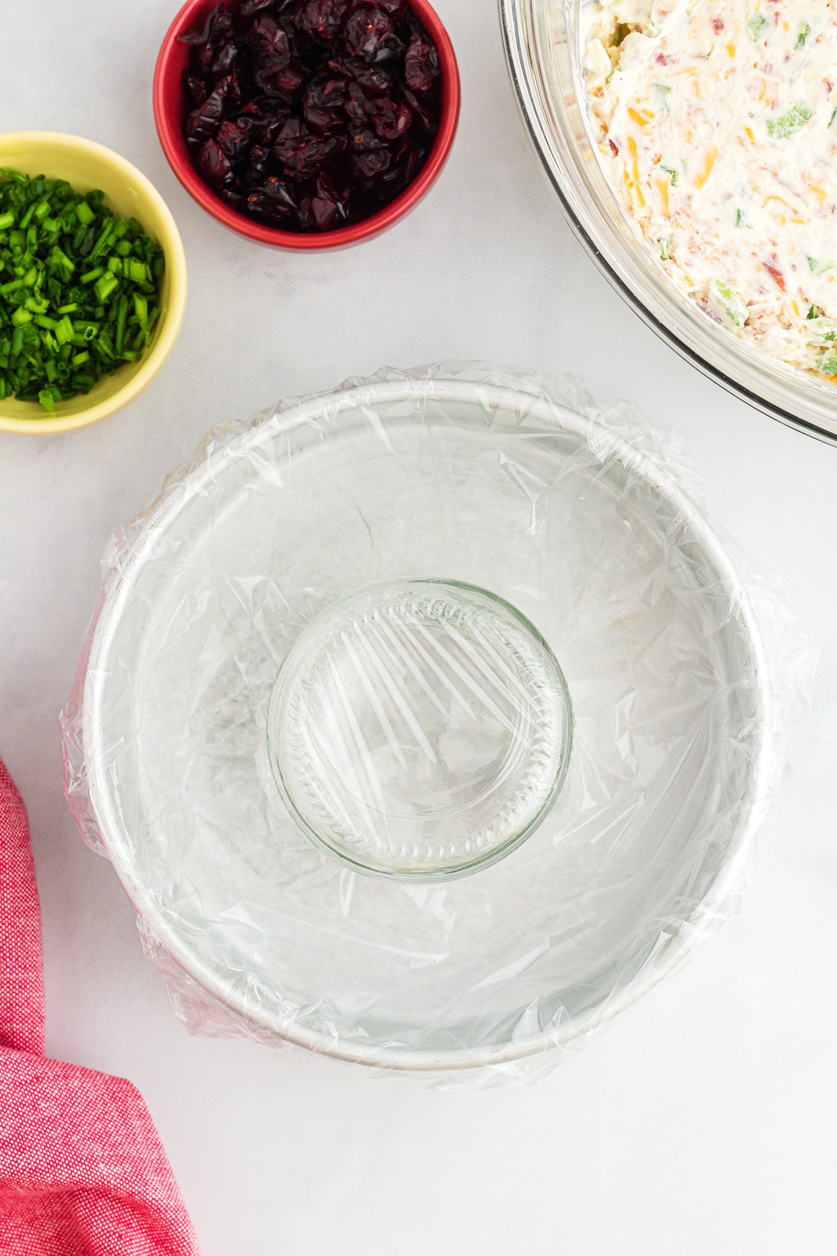 round dish covered in plastic wrap with a drink glass covered in plastic wrap in the center
