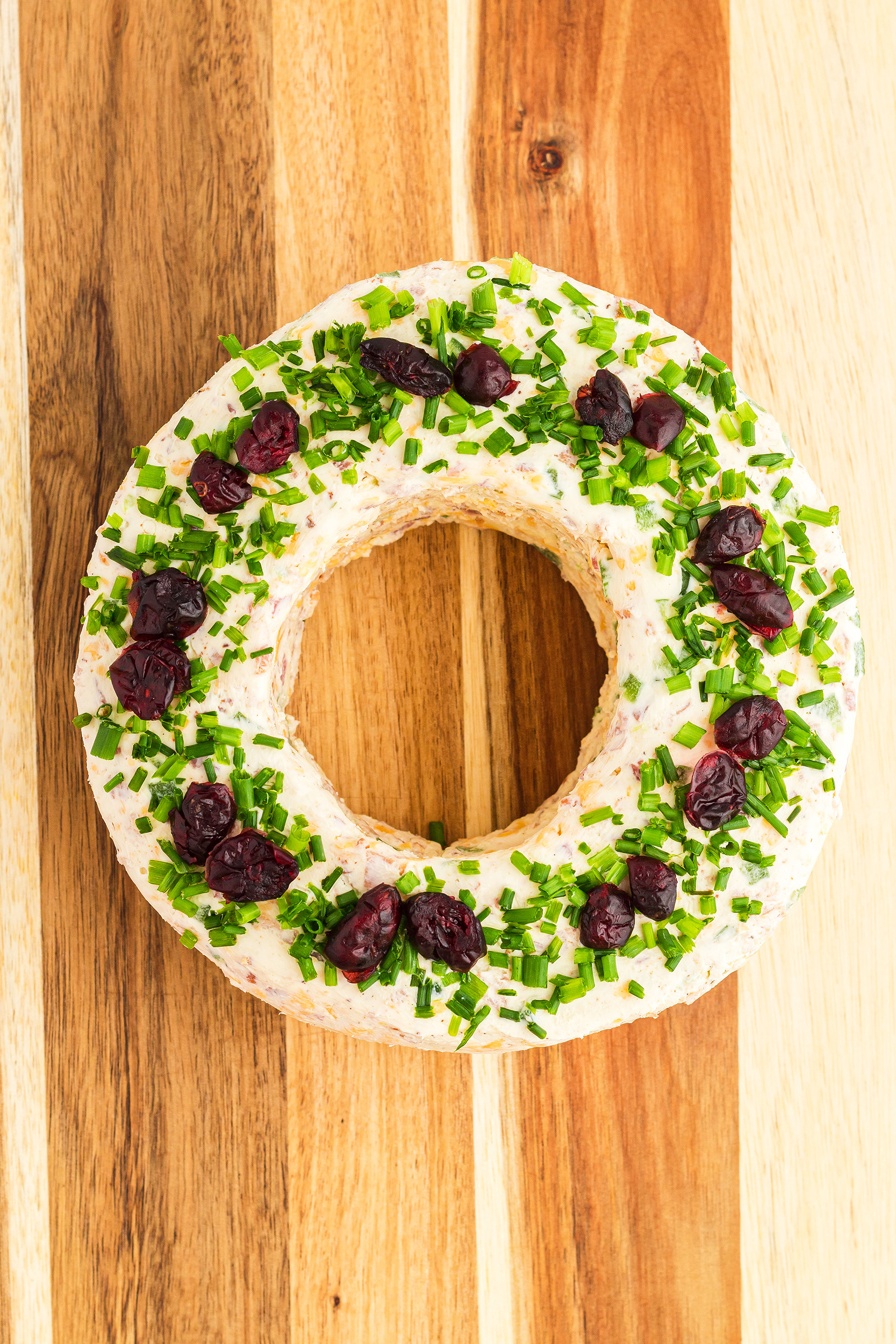 Christmas wreath cheese ball with diced chives and dried cranberries pressed into the top of the wreath