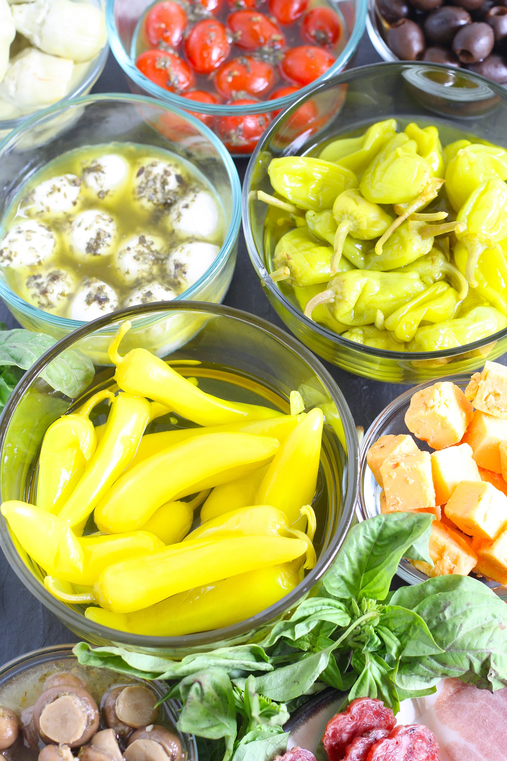 antipasti ingredients like peppers, marinated mozzarella and tomatoes, mushrooms and meat in glass bowls