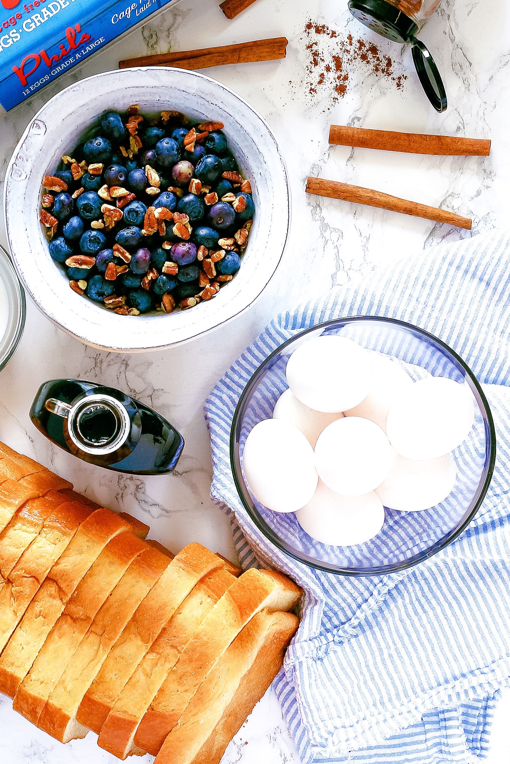 nuts and berries in a bowl, maple syrup, cinnamon sticks, and a bowl of uncooked eggs