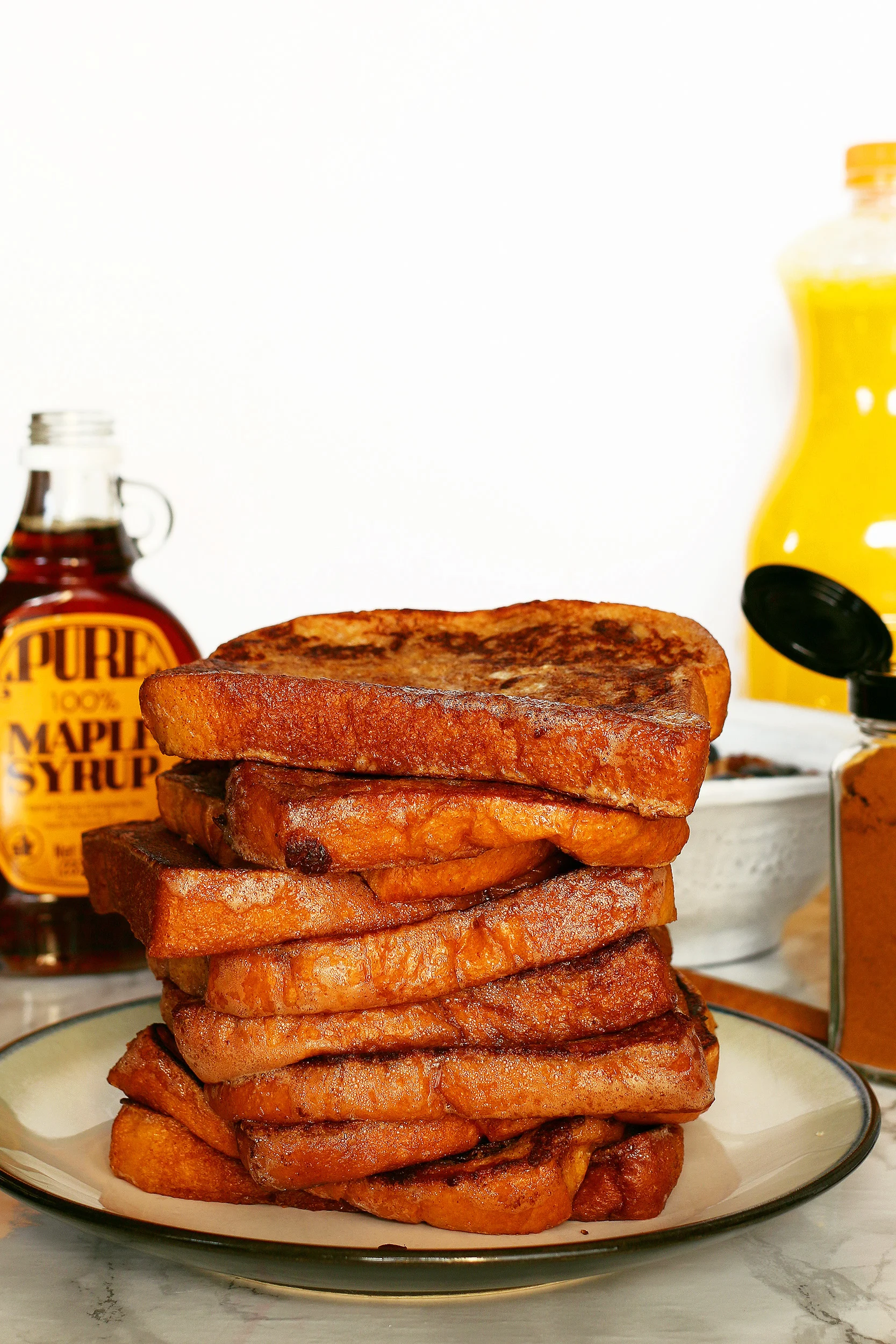 pile of cooked cinnamon French toast on a plate with orange juice and maple syrup in the background