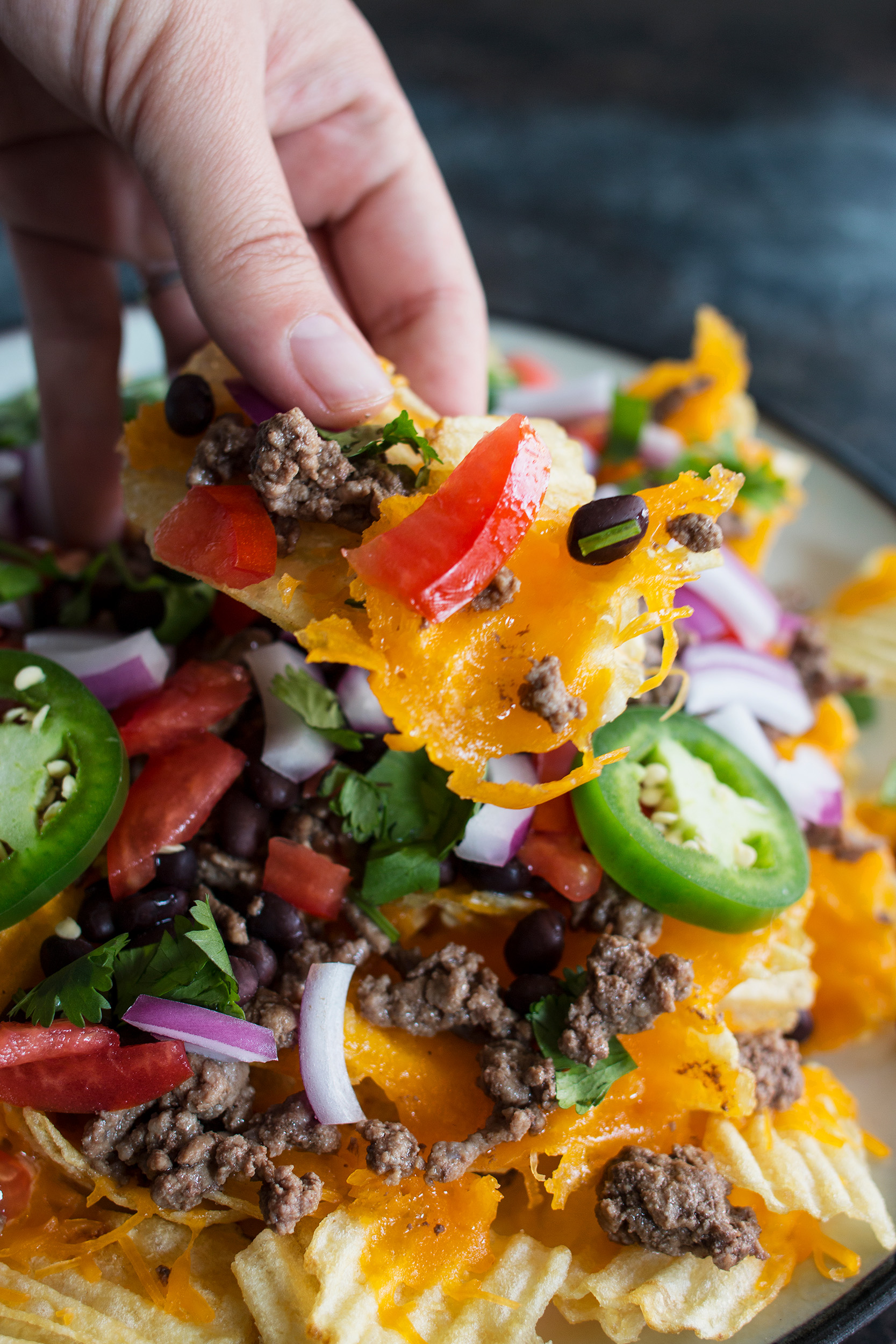 hand holding a chip topped with melted cheese, black beans, and ground beef