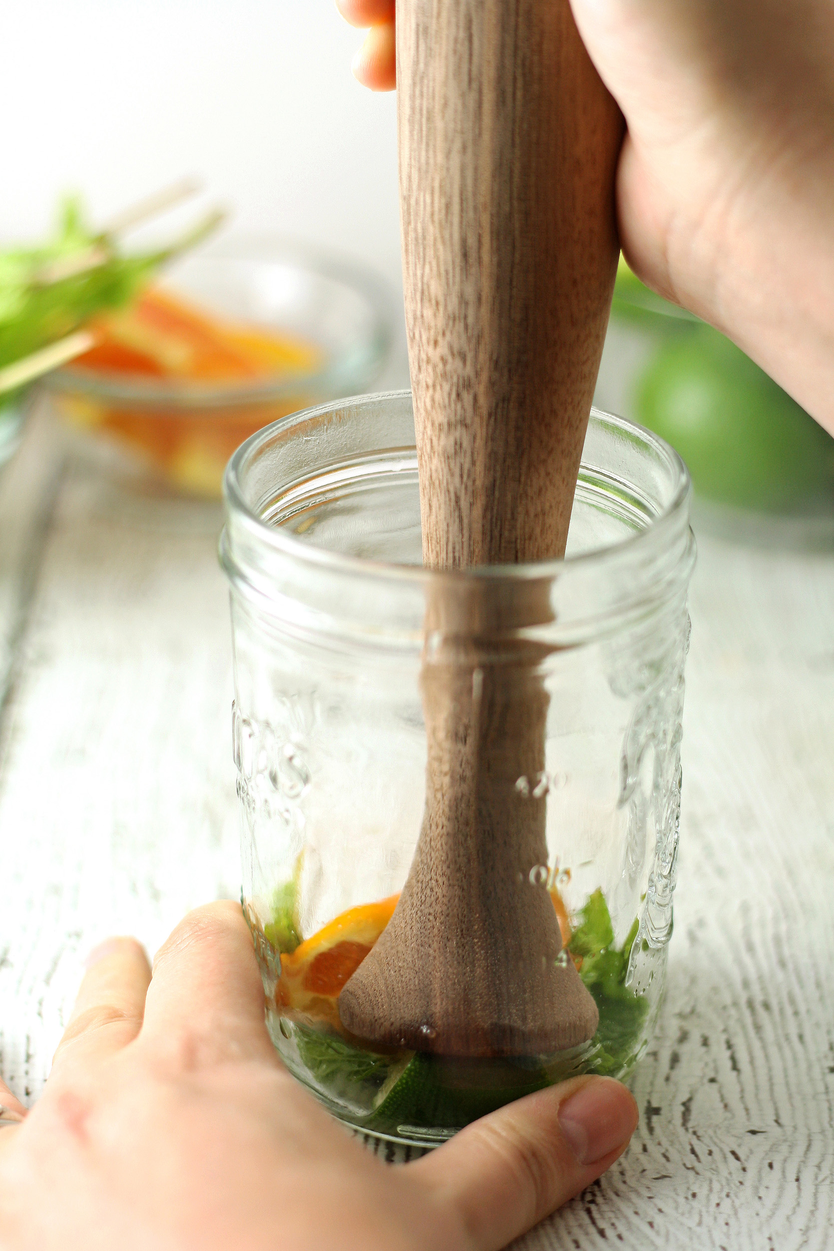 a wooden muddler with mint and an orange wedge in a mason jar