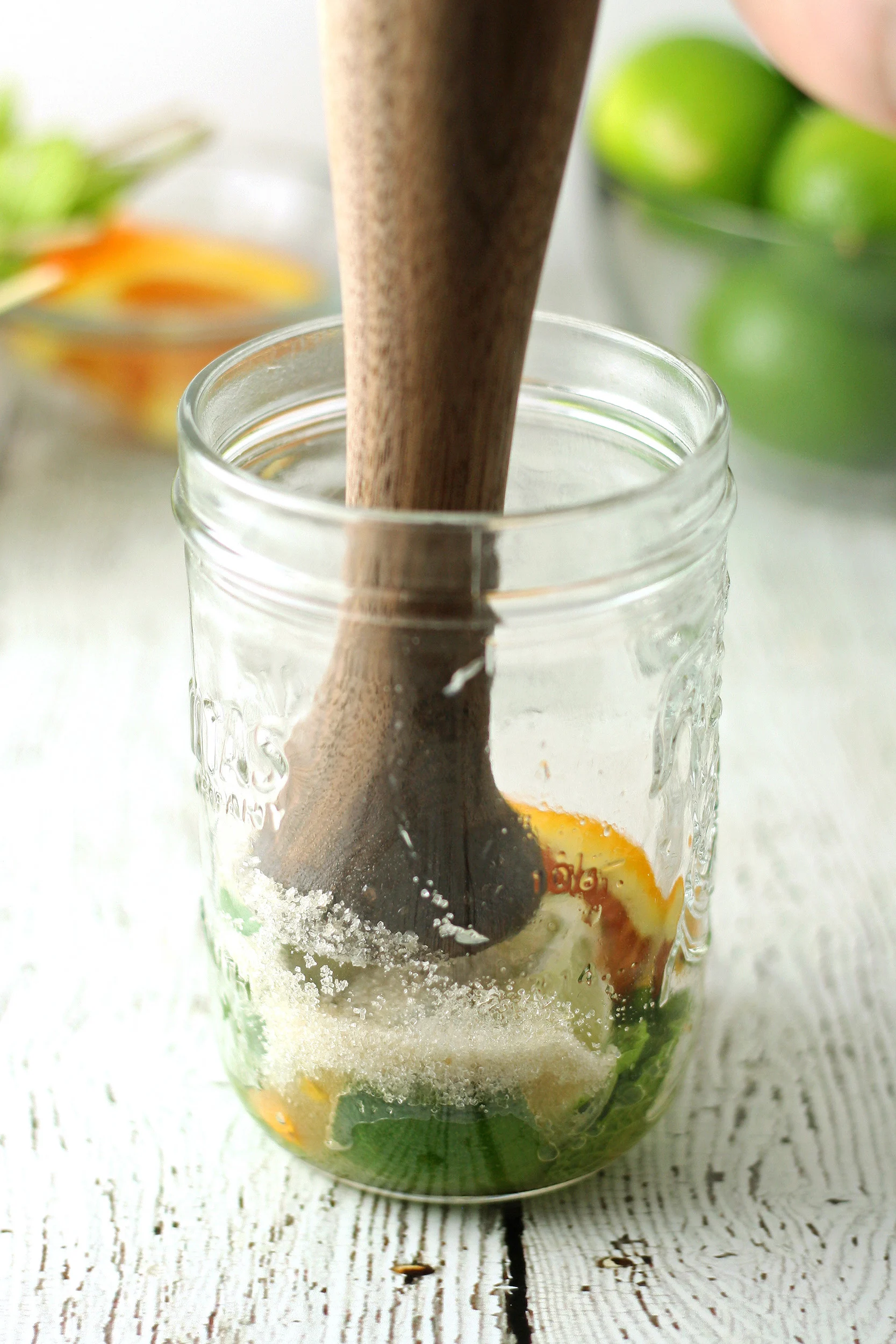 muddling cane sugar and lime juice, mint leaves, and orange slices in a glass