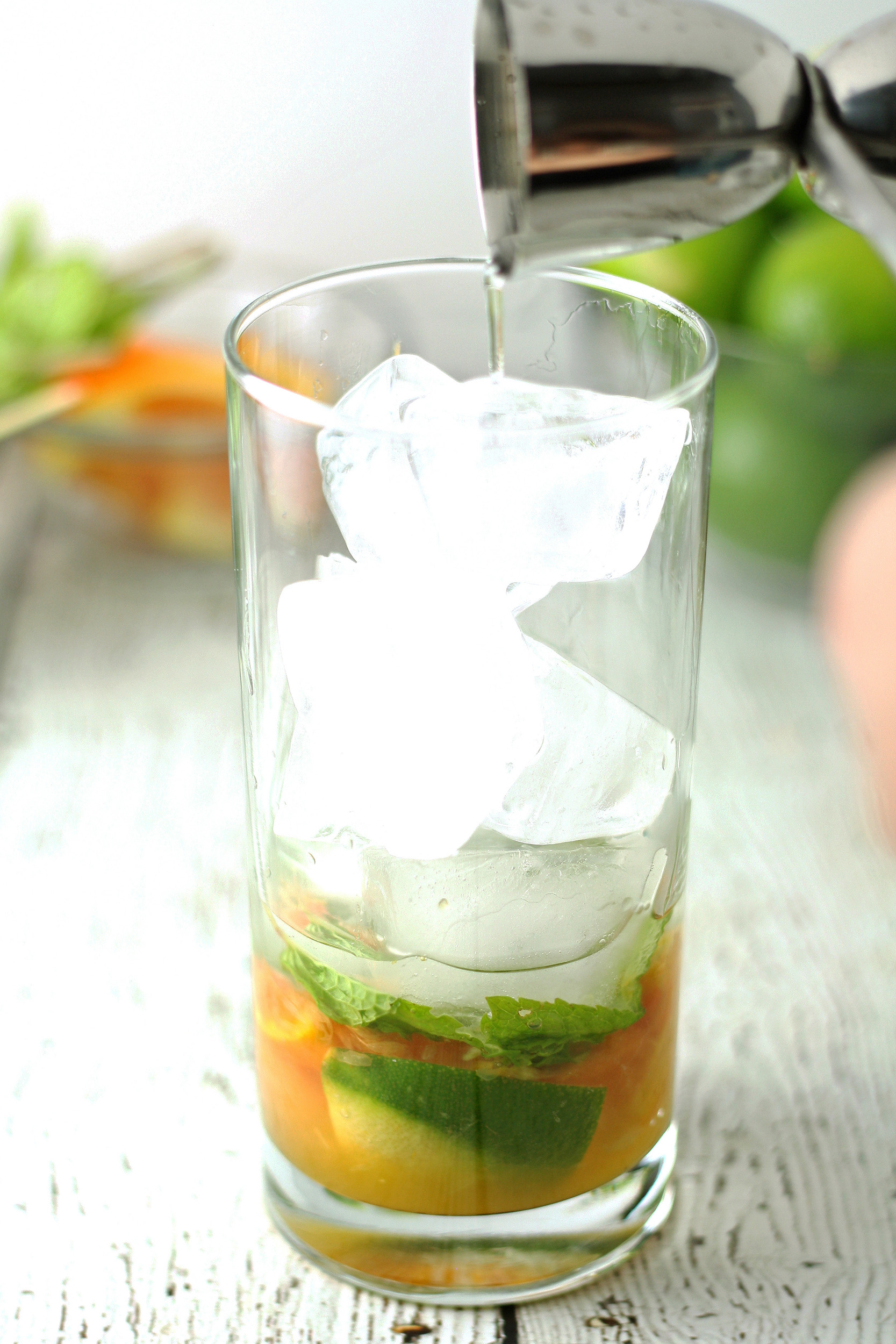 adding rum to a glass with muddle mint, citrus, and ice cubes