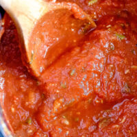 homemade roasted garlic tomato sauce in a pot being stirred with a wooden spoon