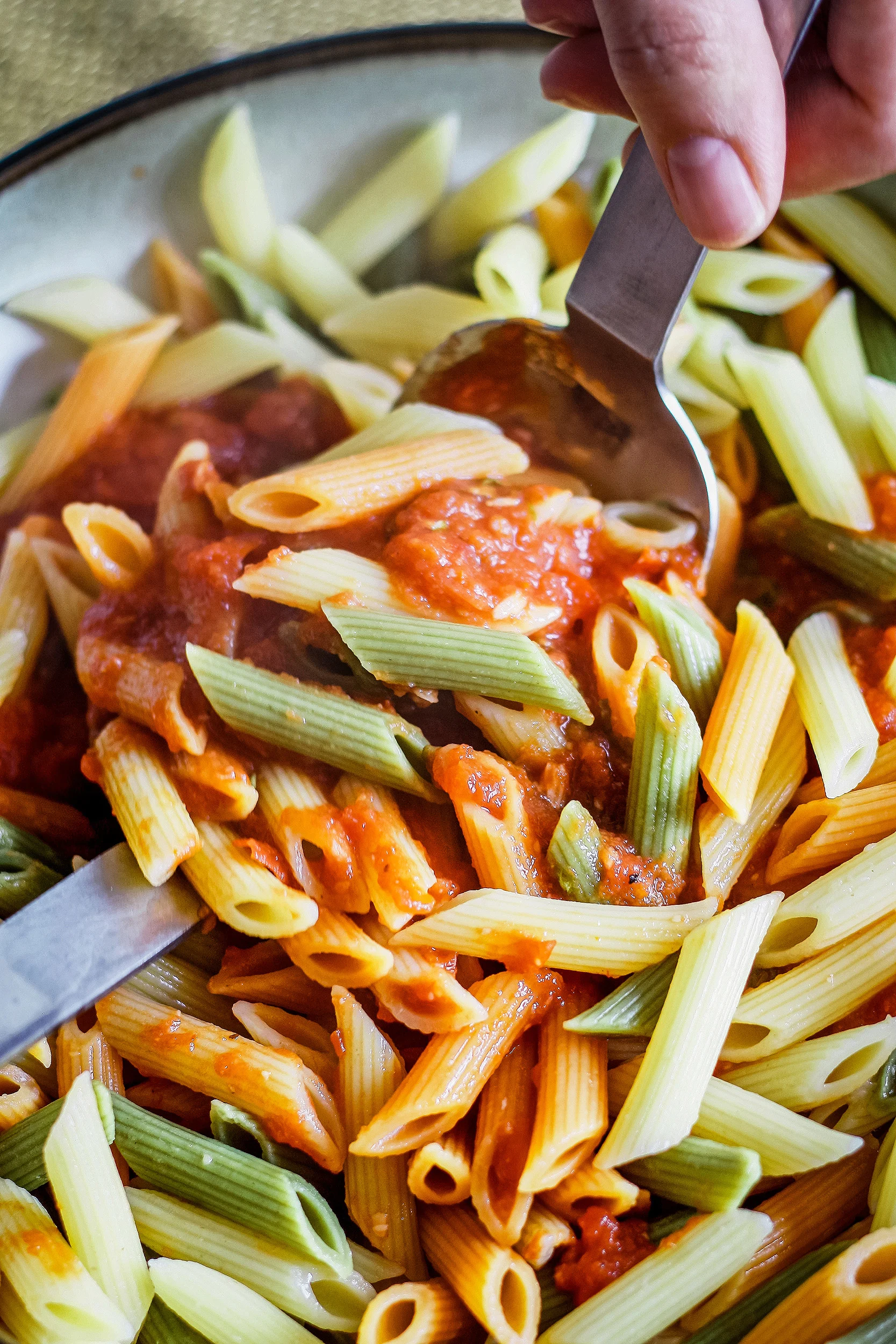 person using two metal serving spoons to toss pasta and pasta sauce