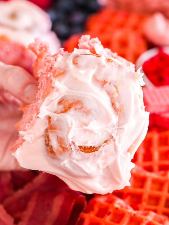 single strawberry cinnamon roll being held by a hand