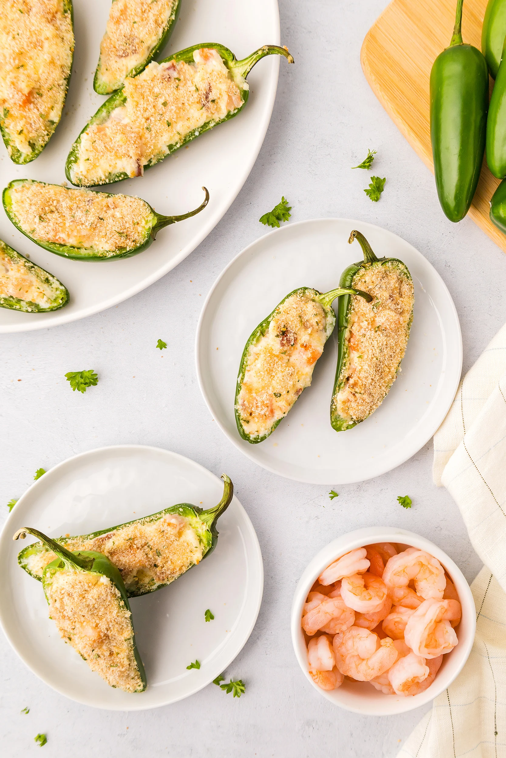 overhead photo of shrimp jalapeño poppers on small plates, fresh jalapeños on a cutting board, and a bowl of cooked shrimp