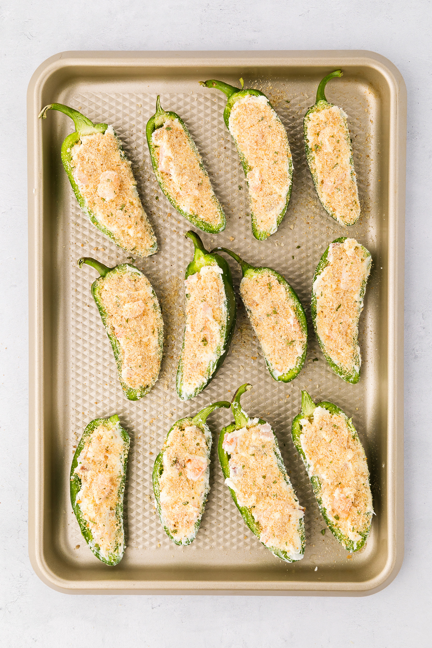 uncooked shrimp stuffed jalapeños topped with bread crumbs on a sheet pan