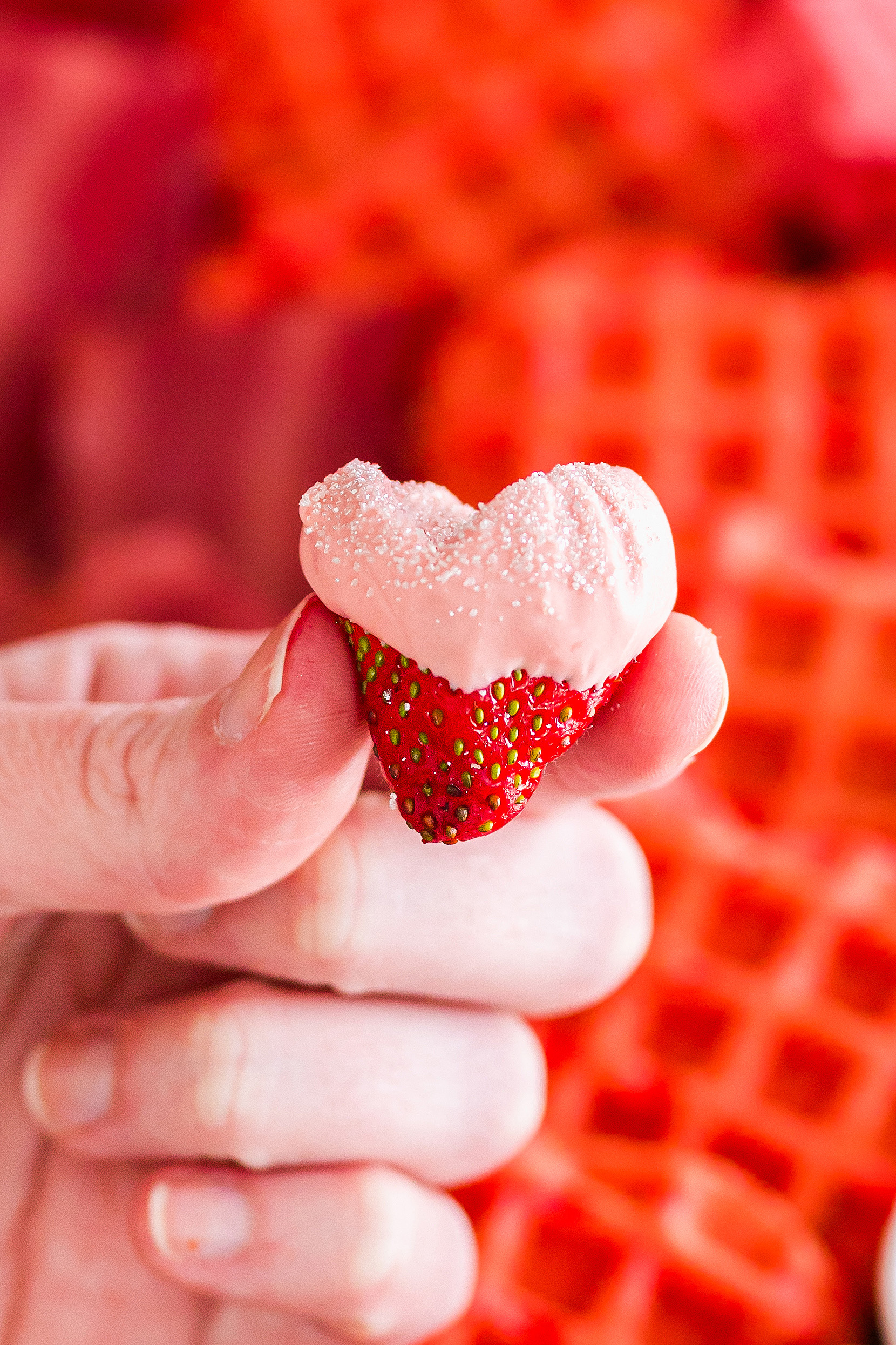 a hand holding a heart shaped strawberry dipped in pink frosting