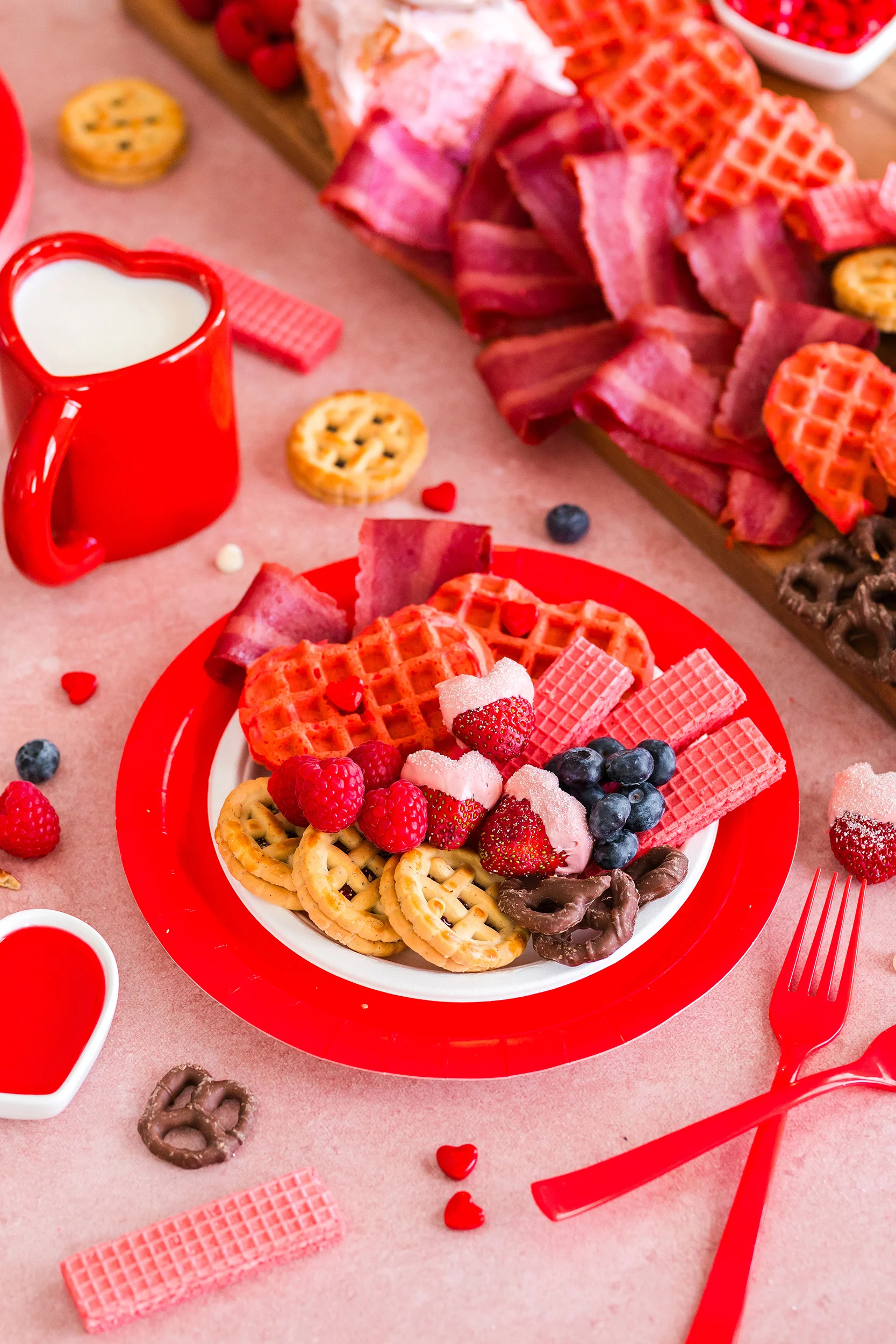 red plate with different items from the Valentine's Day breakfast charcuterie board and a heart shaped mug of milk