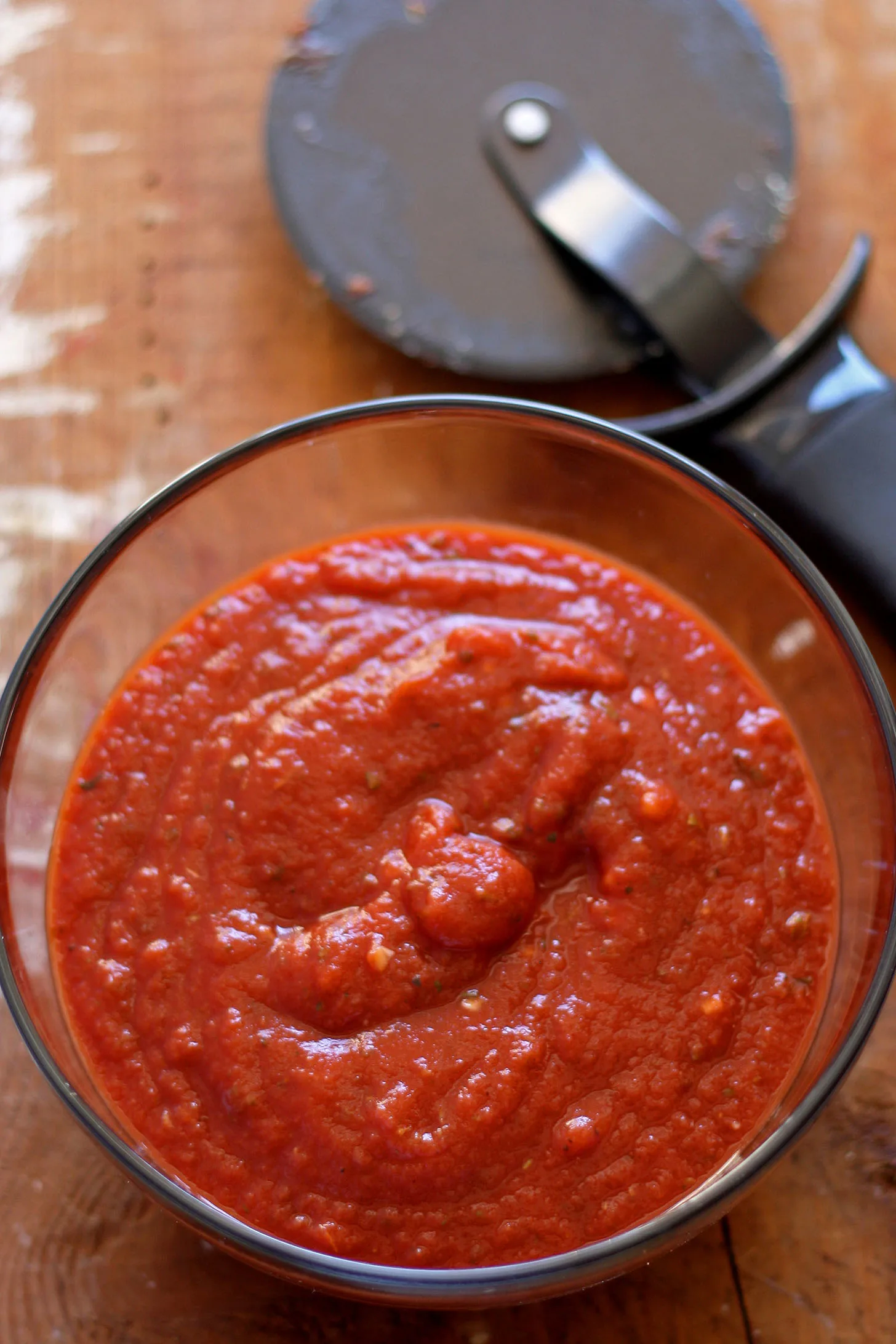 overhead photo of a bowl of homemade pizza sauce with a pizza cutter in the background