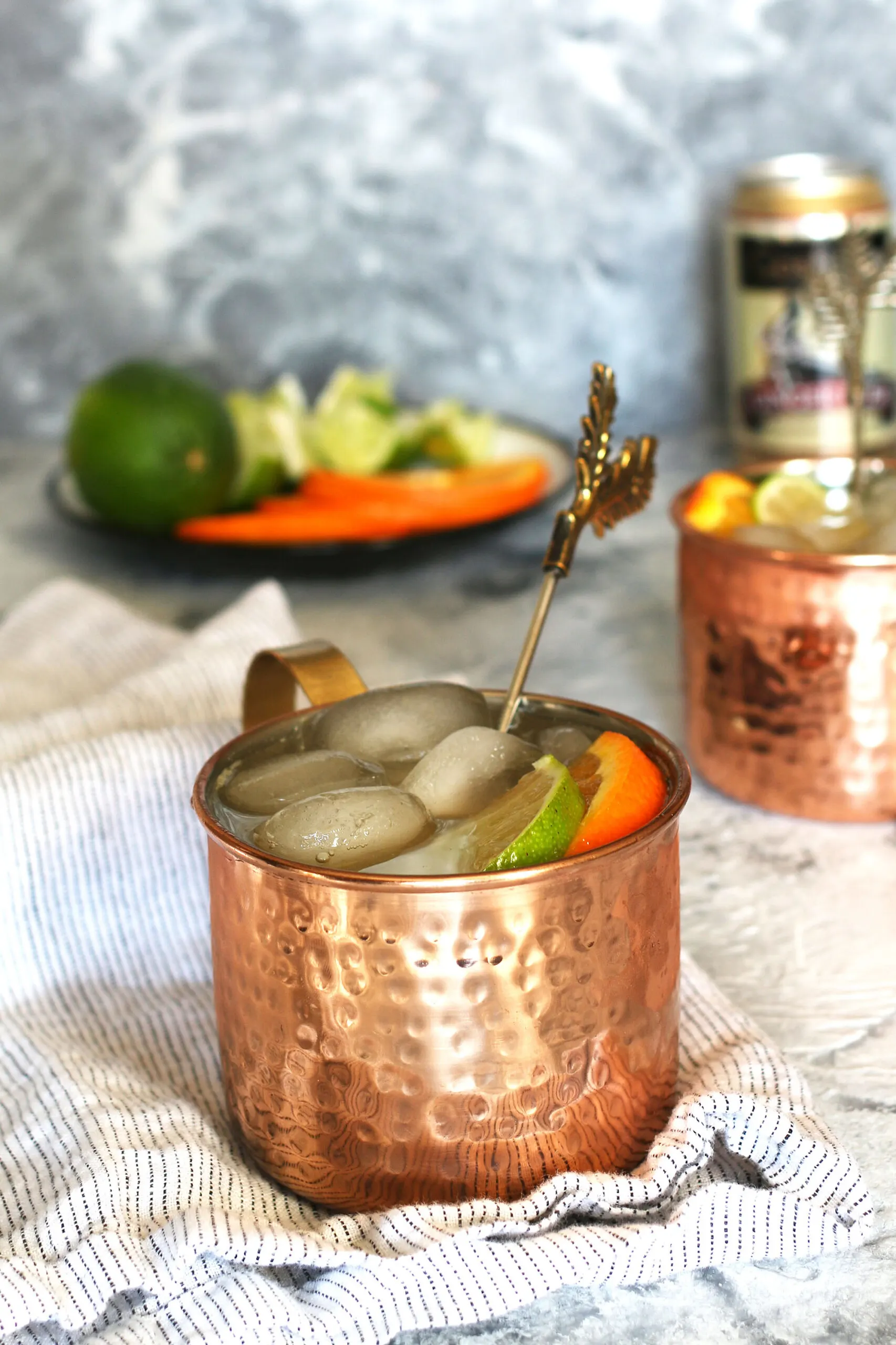 an orange Moscow Mule cocktail on a white napkin with ginger beer and mule garnishes in the background